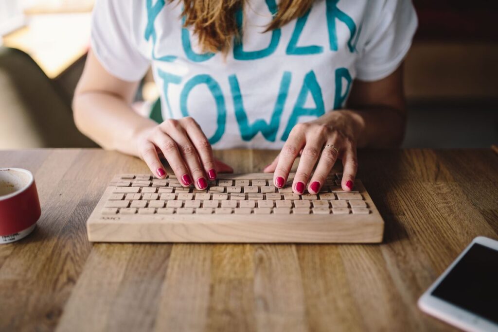 Closeup of female hands typing text on a wireless wooden keyboard Stock Free