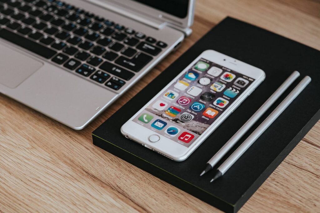 Silver Acer laptop, a white Apple iPhone and a notepad on a wooden desk Stock Free