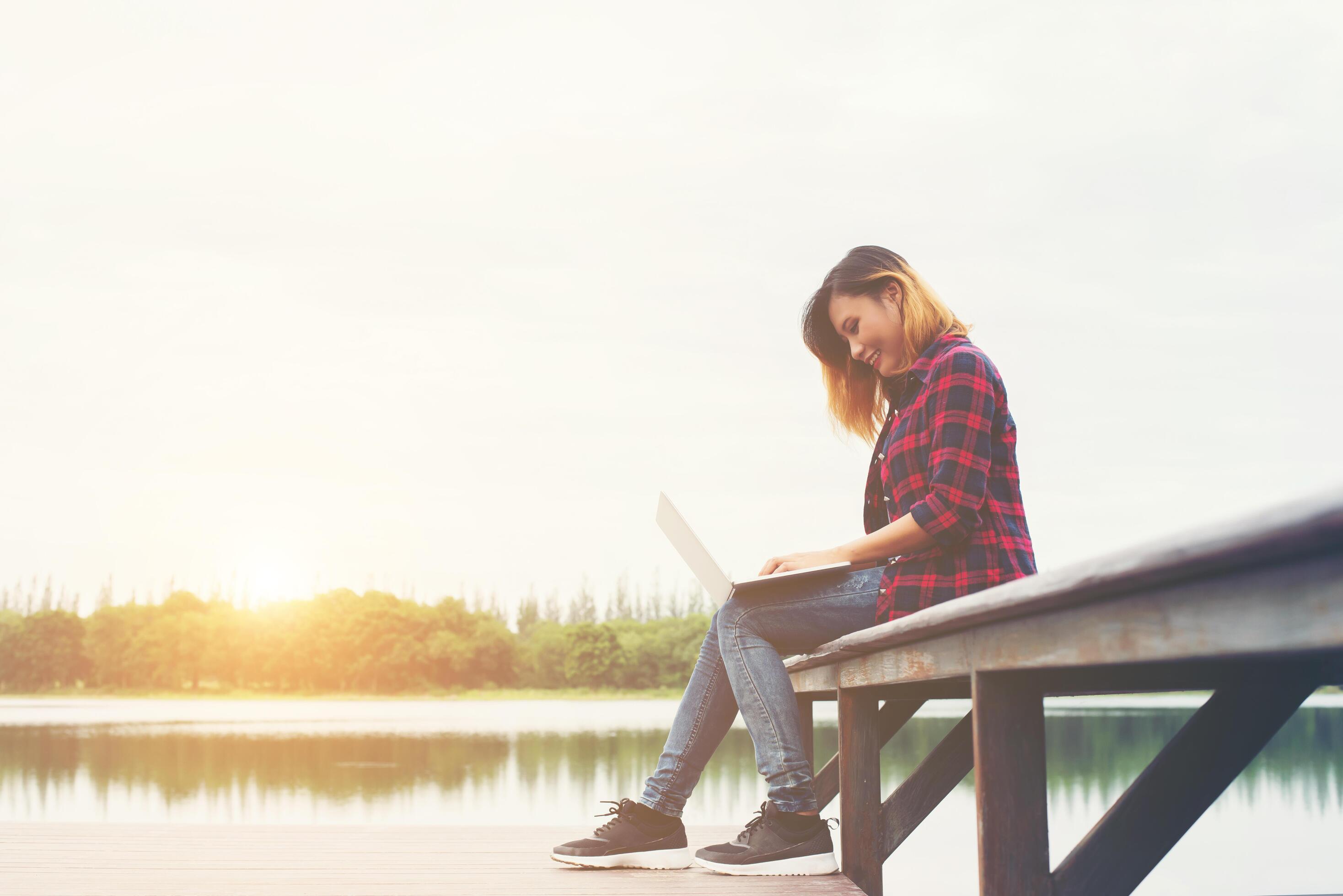 Young happy hipster woman working with her laptop sitting on pier,relaxing enjoy with nature. Stock Free