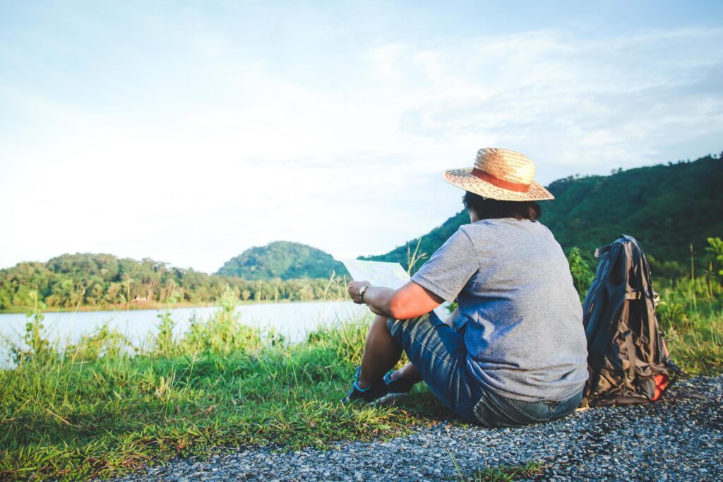 A senior Asian woman is wearing a hat sitting on the grass to see a map of nature tourism. The concept of health tourism for the elderly Stock Free