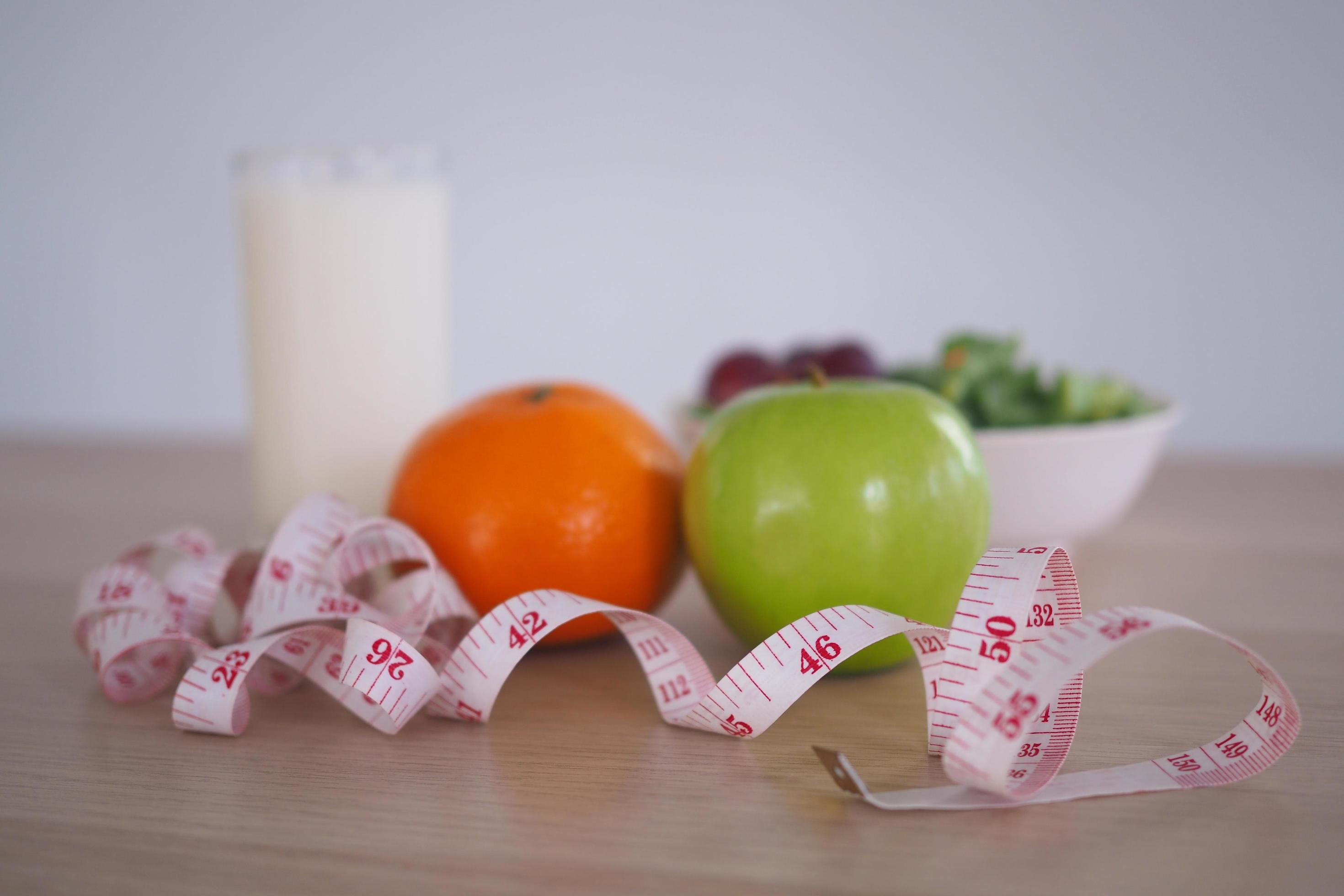 Focus at measuring tape – Healthy food with vegetable salad, orange, apple and milk. Concept Diet Stock Free