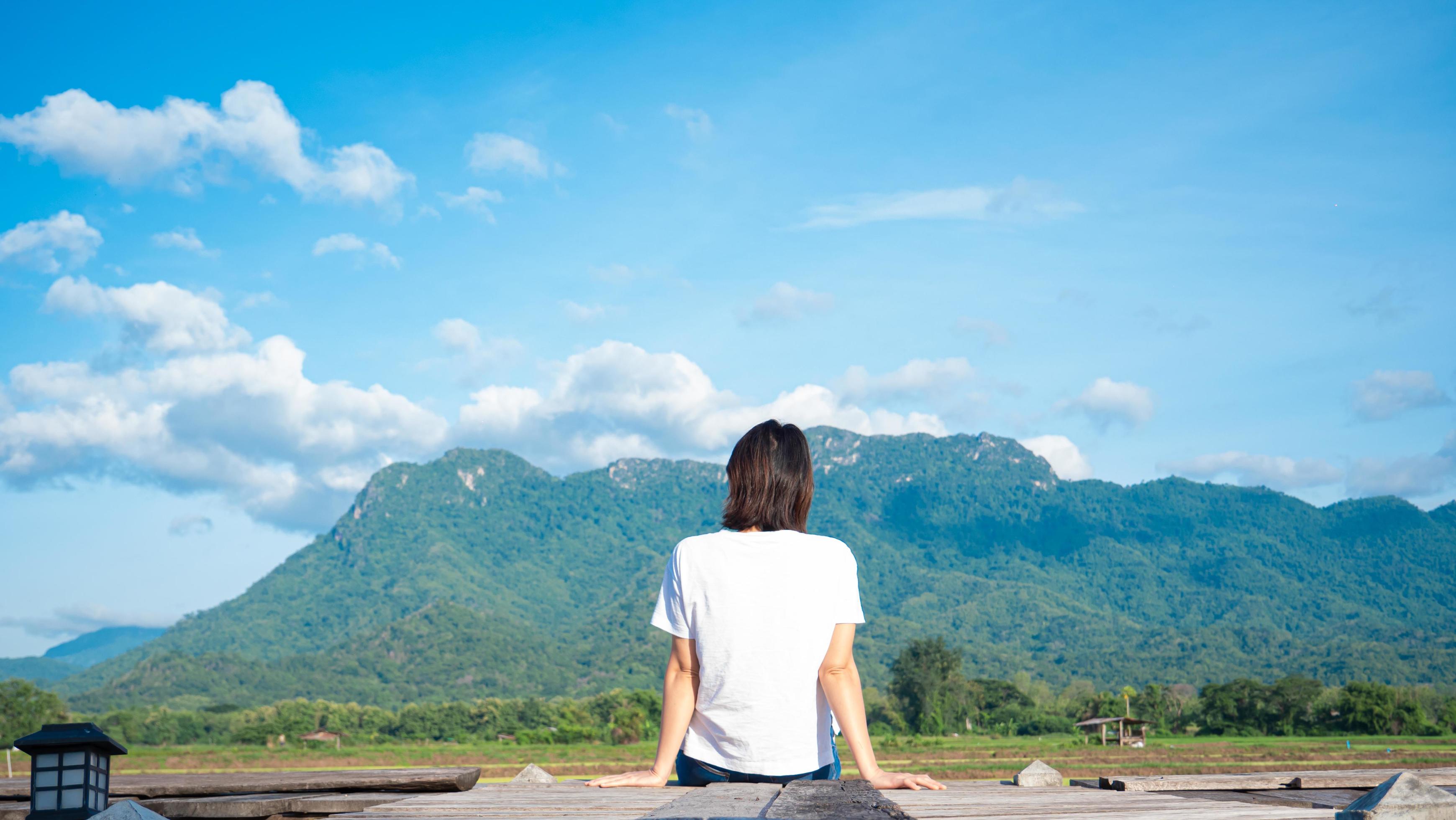 girl wearing a casual t-shirt Sit on a wooden walkway, see nature, mountains, rice fields, fresh air. and the morning sun bright blue sky white clouds Stock Free