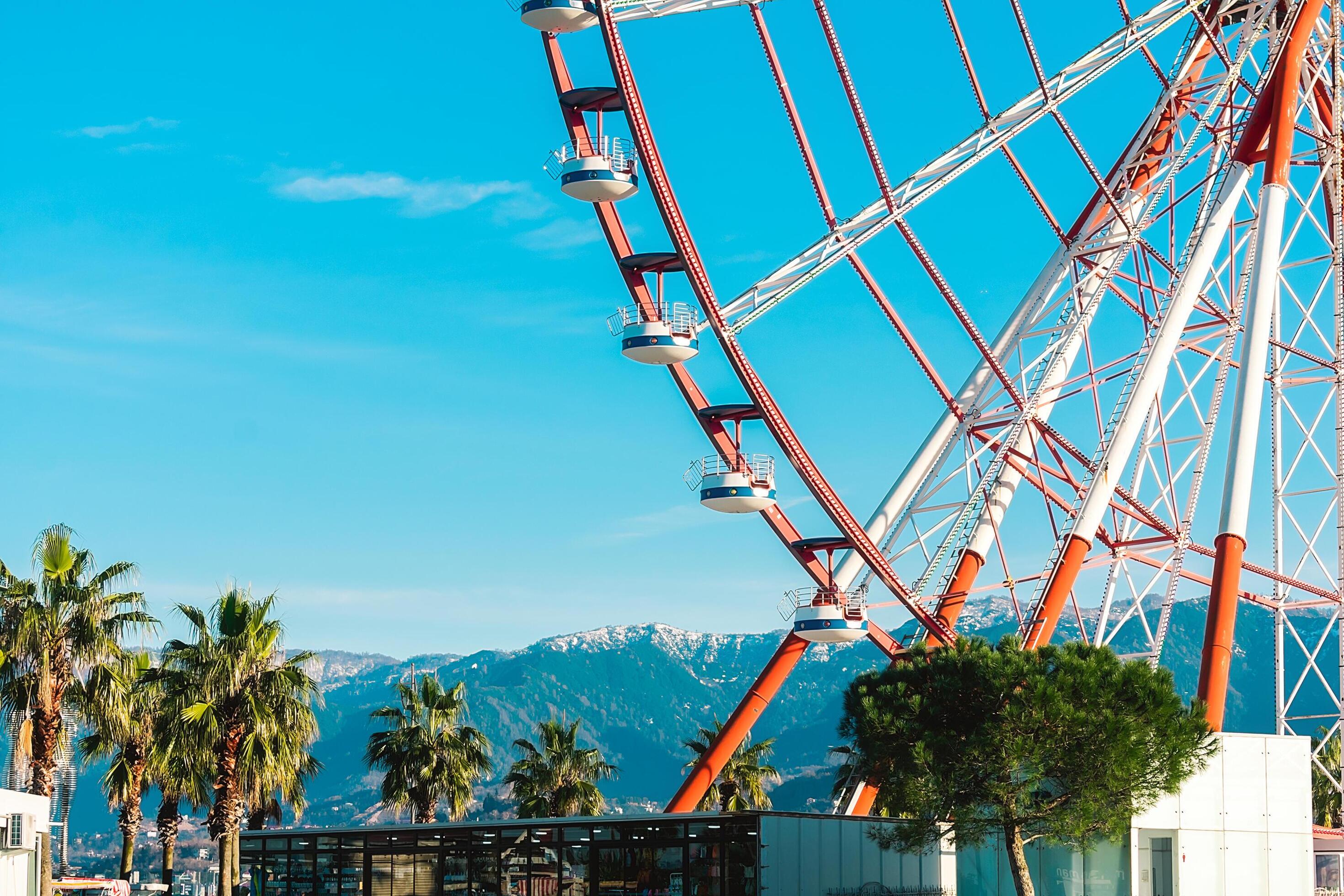 View of the Ferris wheel attraction against a background of blue sky between palm trees. Ferris wheel in the Georgian city of Batumi. Stock Free