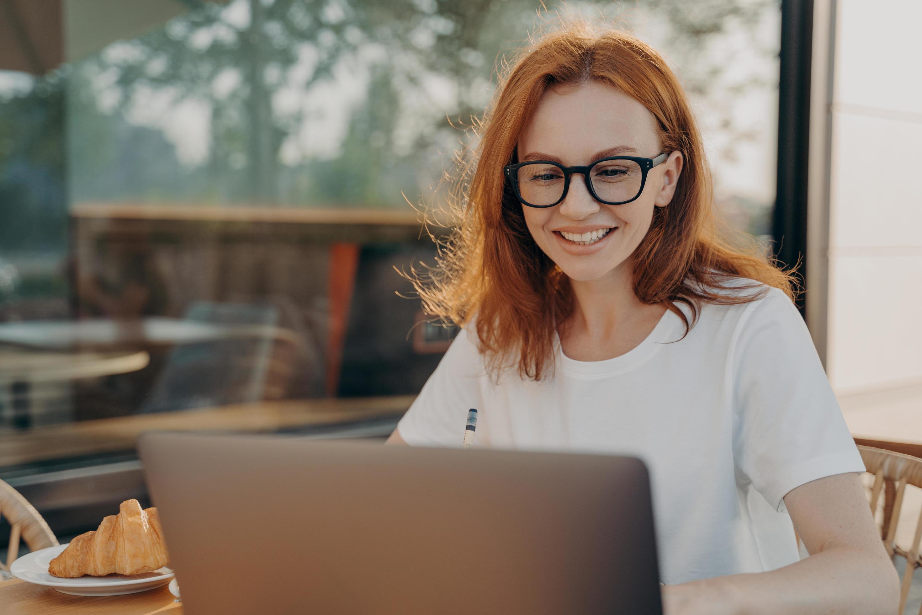 Beautiful redhead professional woman freelancer works on laptop computer poses in outdoor cafe Stock Free