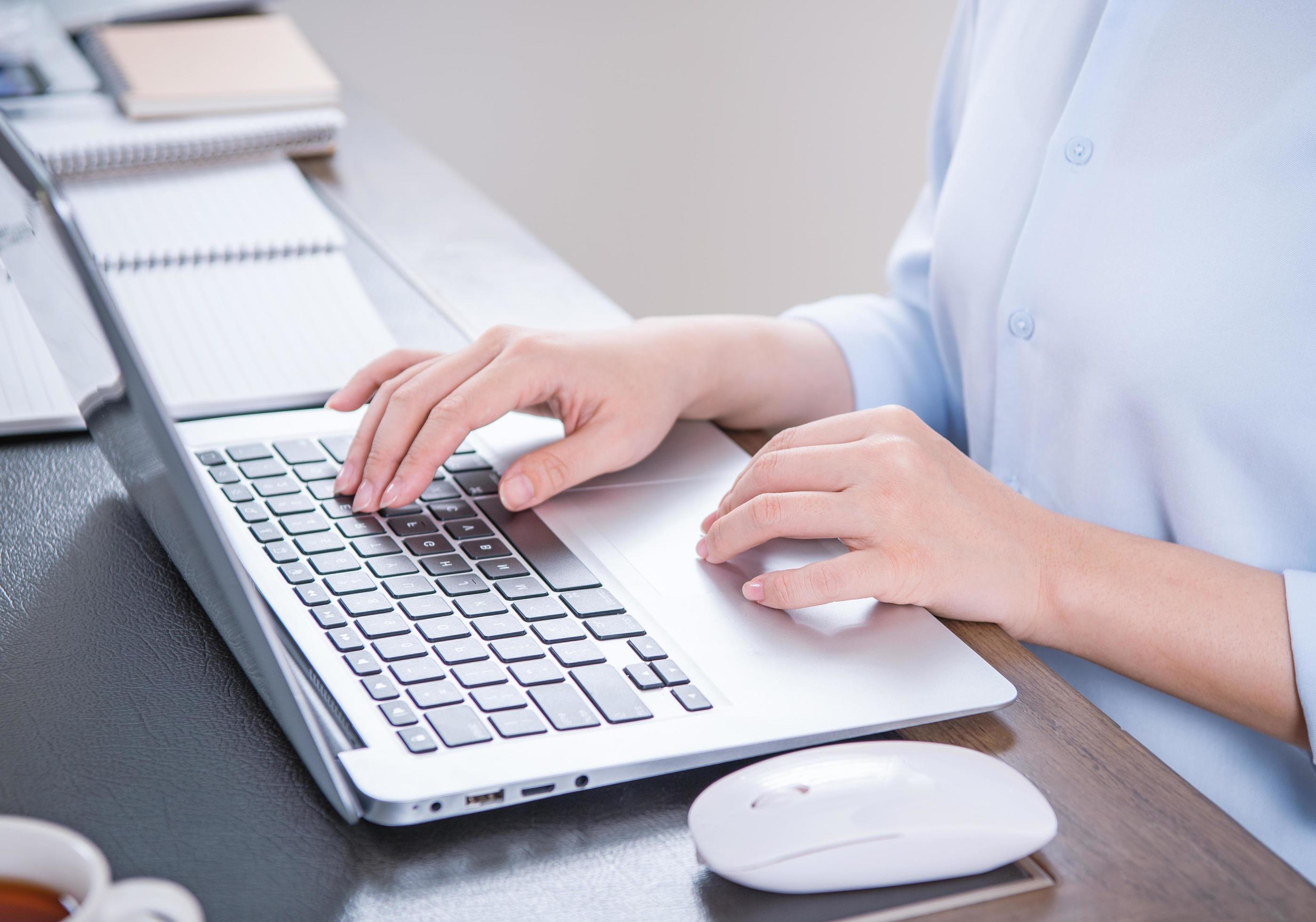 Business concept. Woman in blue shirt typing on computer with coffee on office table, backlighting, sun glare effect, close up, side view, copy space Stock Free