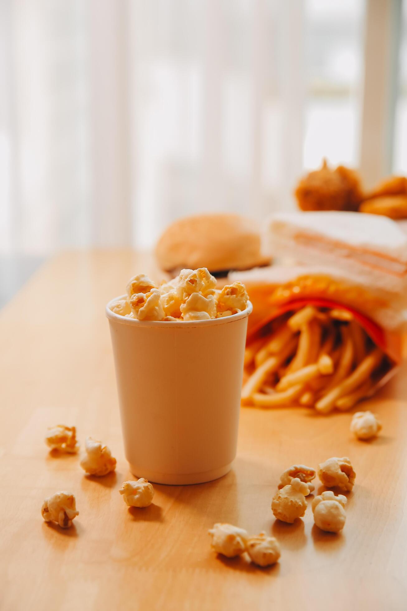 A bucket of popcorn, top-view, warm colors, light brown wooden background, flat lay, daylight macro close-up Stock Free