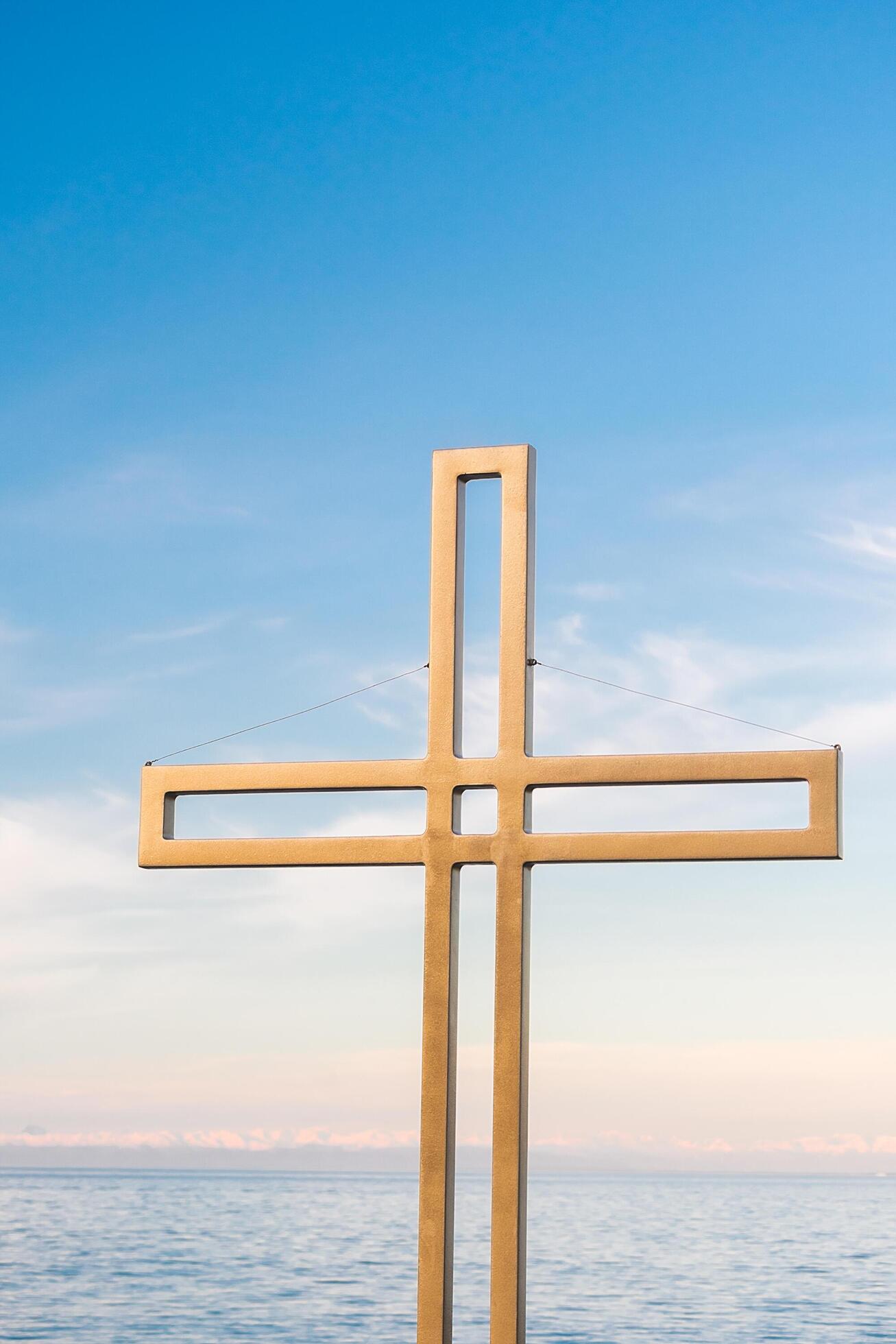 Golden cross against a background of blue sky with clouds. A minimalistic view of a gold-colored cross against the sky. Stock Free