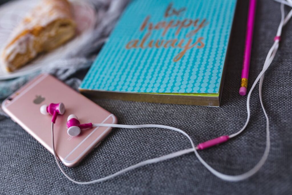 Blue notebook with a pink iPhone, headphones and a sweet bun Stock Free