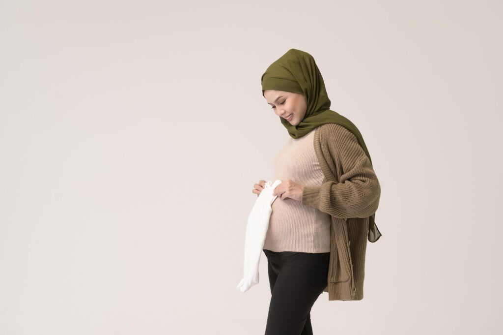 Portrait of Pregnant muslim woman in hijab holding baby cloth over white background studio Stock Free