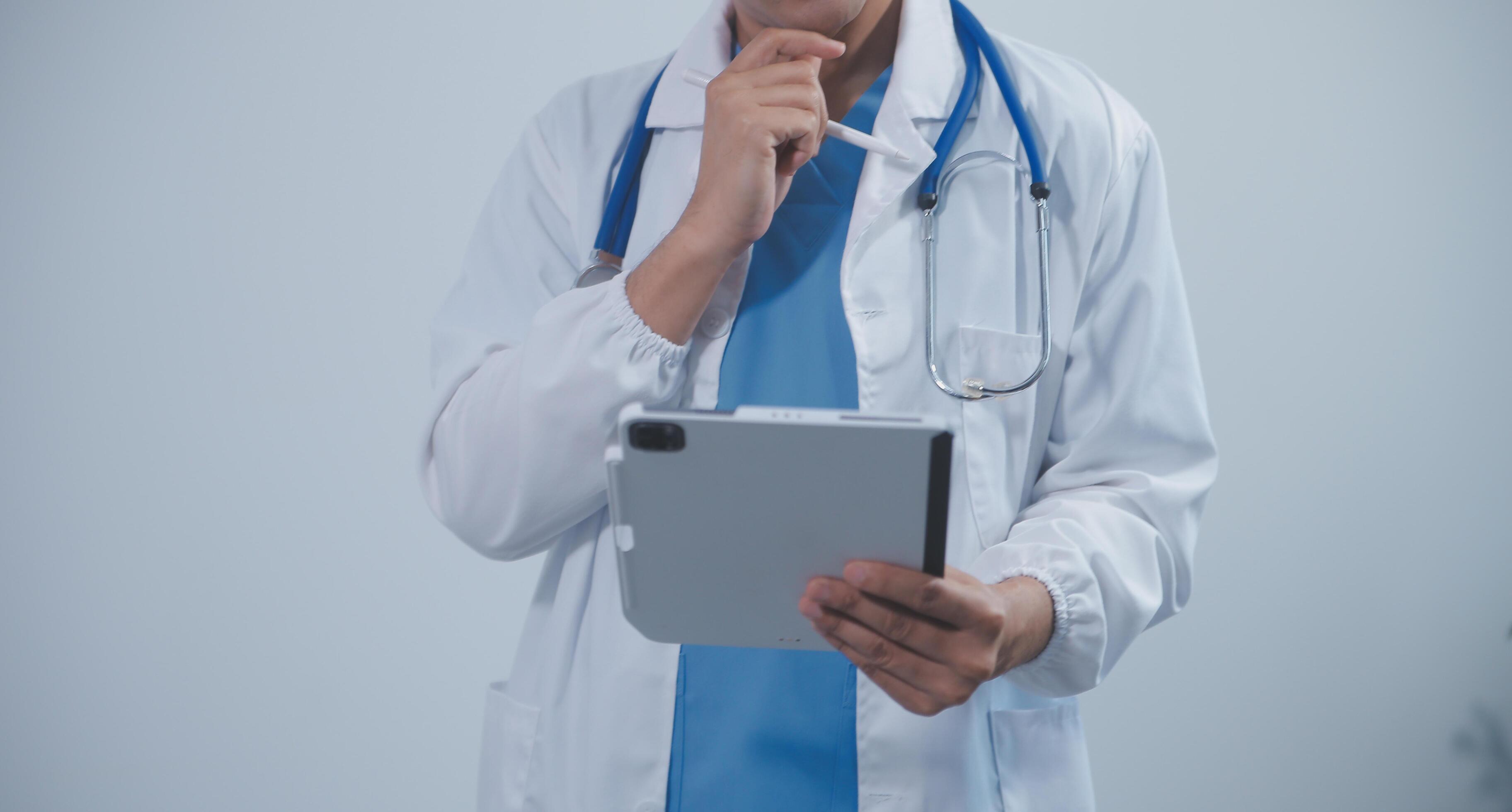 Mature male doctor with tablet pc is giving presentation. Blurred background indoors. Stock Free