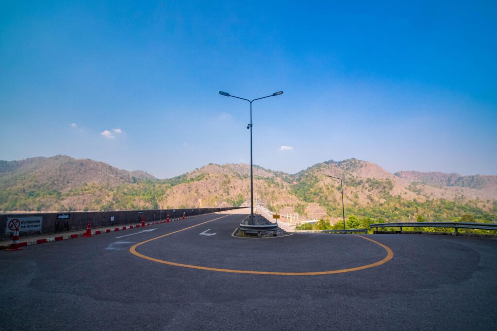 The scene of the road at the top of the dam, with the mountains in the background and a light pole. Stock Free