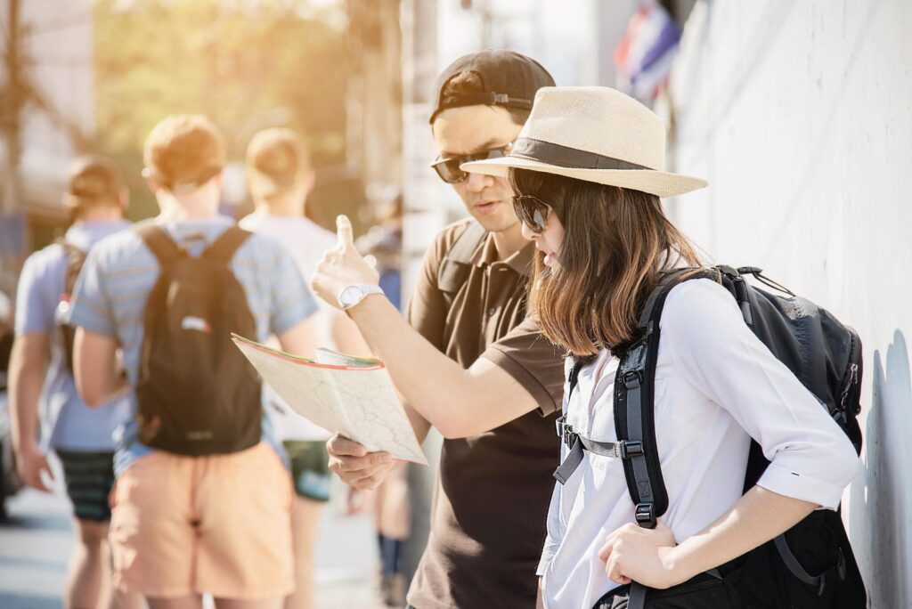 Asian backpack couple tourist holding city map crossing the road – travel people vacation lifestyle concept Stock Free