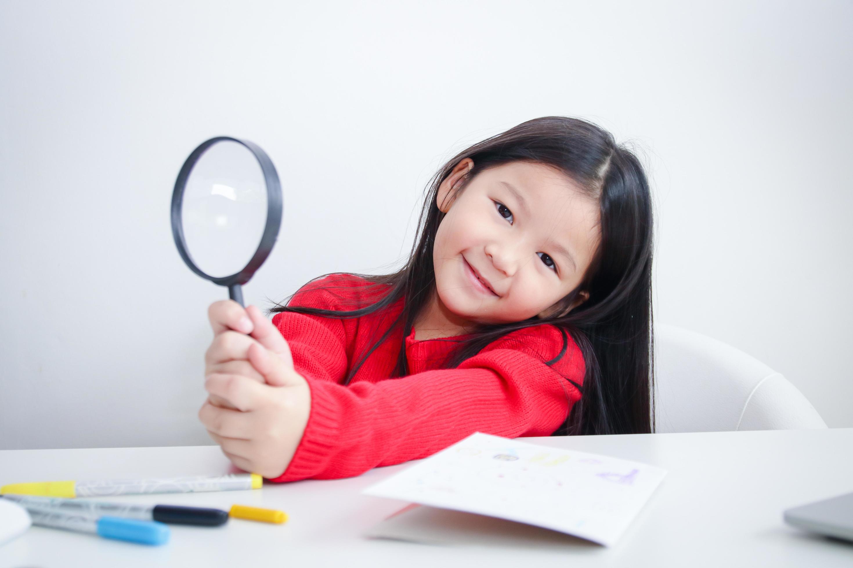 Cute Asian girl holding a magnifying glass on the study desk. Concept of educational development. Stock Free