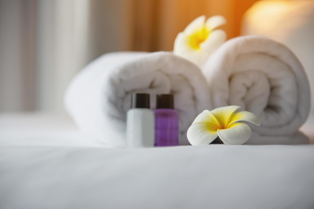 Hotel towel and shampoo and soap bath bottle set on white bed with plumeria flower decorated – relax vacation at the hotel resort concept Stock Free