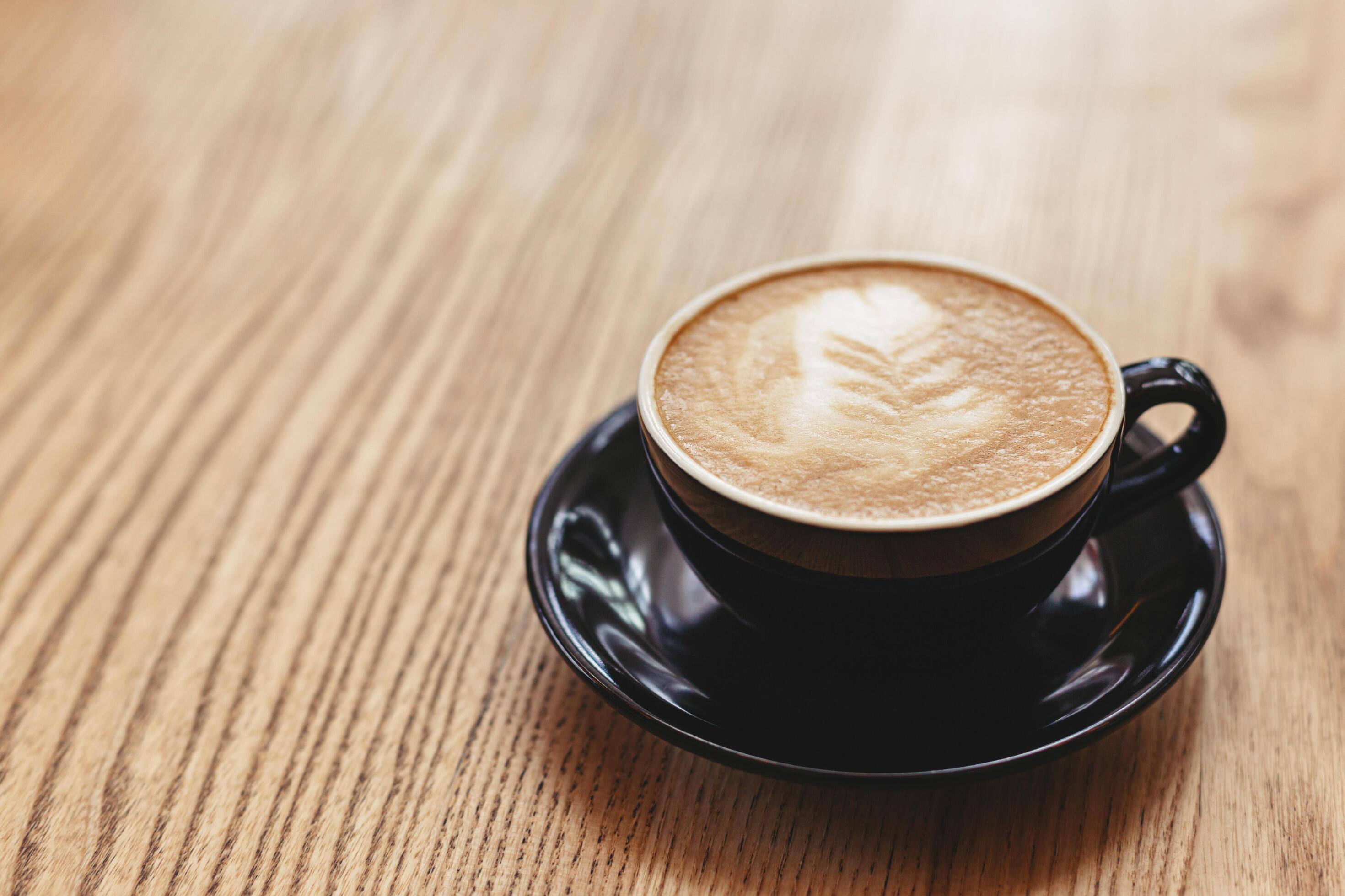 Cup of cappuccino with latte art on wooden background. Black ceramic cup, place for text. Stock Free