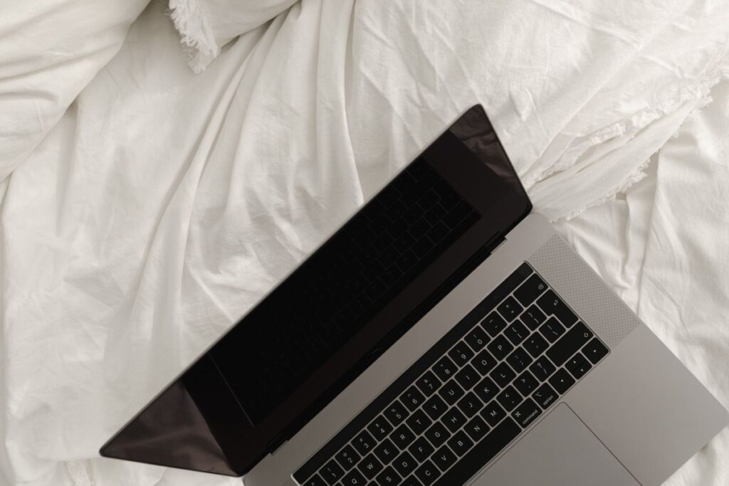 Working with a laptop in bed – white cotton bedding Stock Free