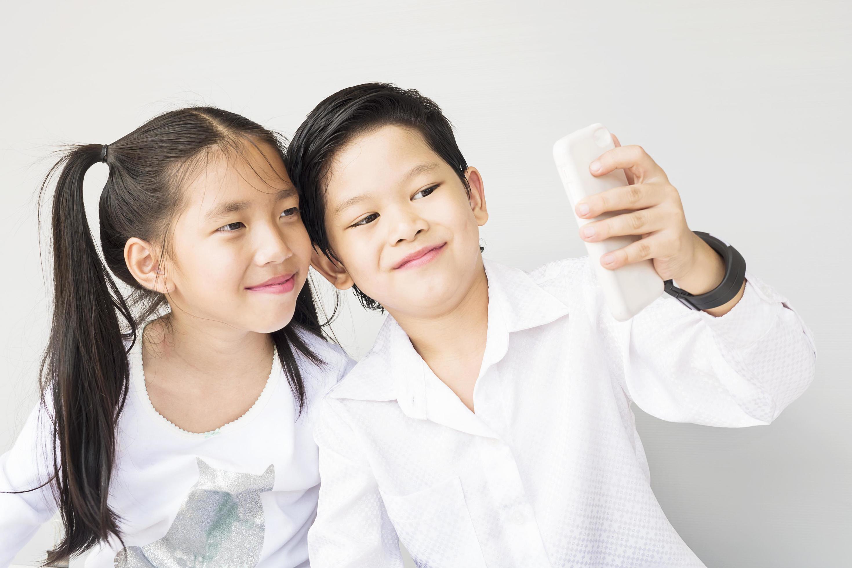 Lovely Asian couple school kids are taking selfie, 7 and 10 years old, over gray background Stock Free