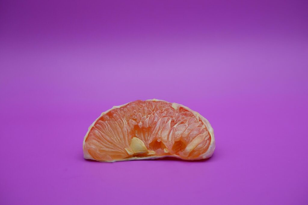 a slice of grapefruit isolated on a purple background. grapefruit that has been peeled until the grain of the orange is visible Stock Free