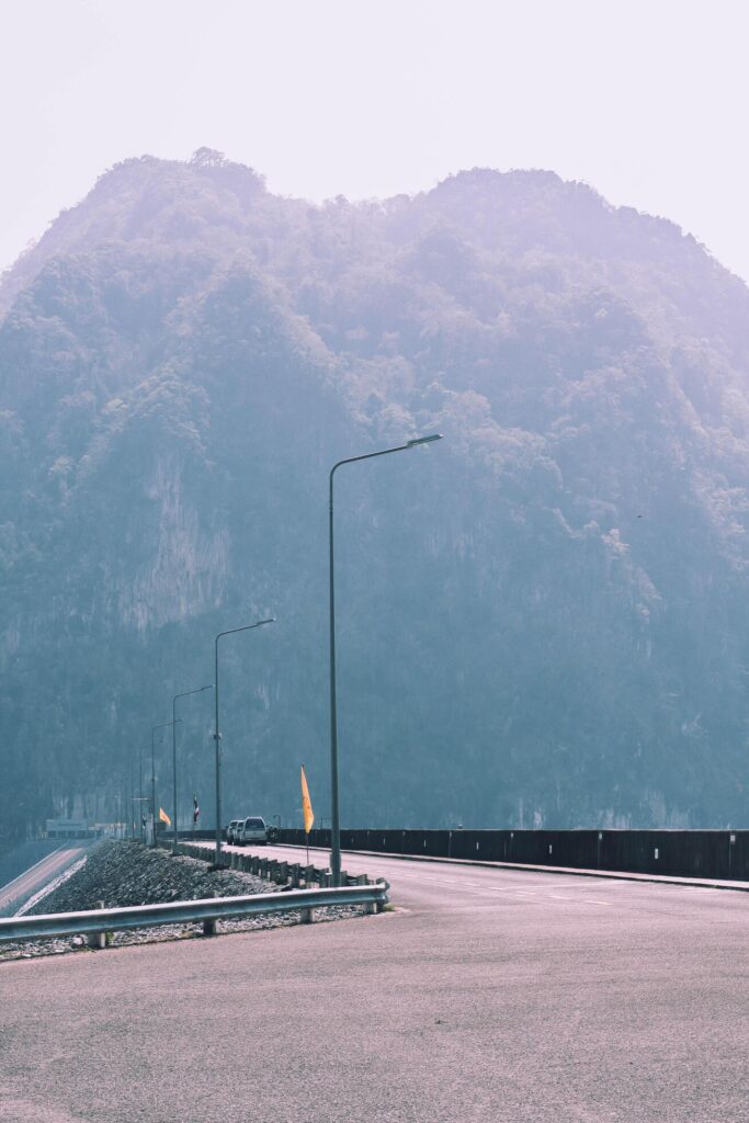 The scene of the road at the top of the dam, with the mountains in the background and a light pole. Stock Free