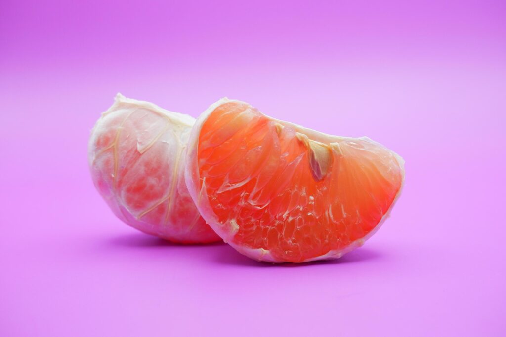 2 grapefruit isolated on purple background. 2 pieces of grapefruit that have been peeled until the grain of the orange is visible Stock Free