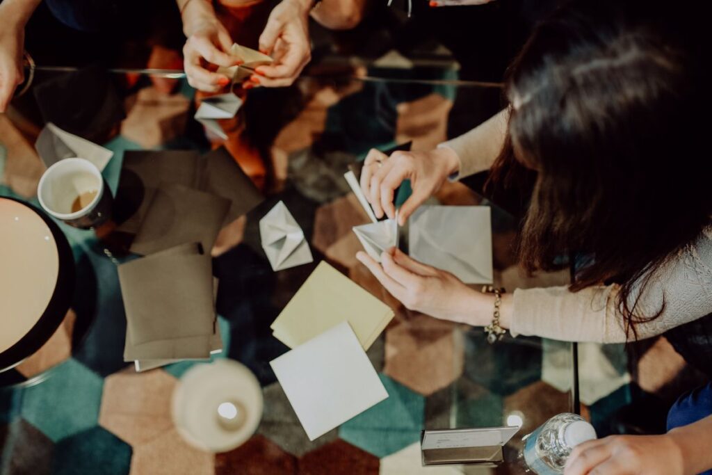 Women folding sheet of paper while making origami Stock Free