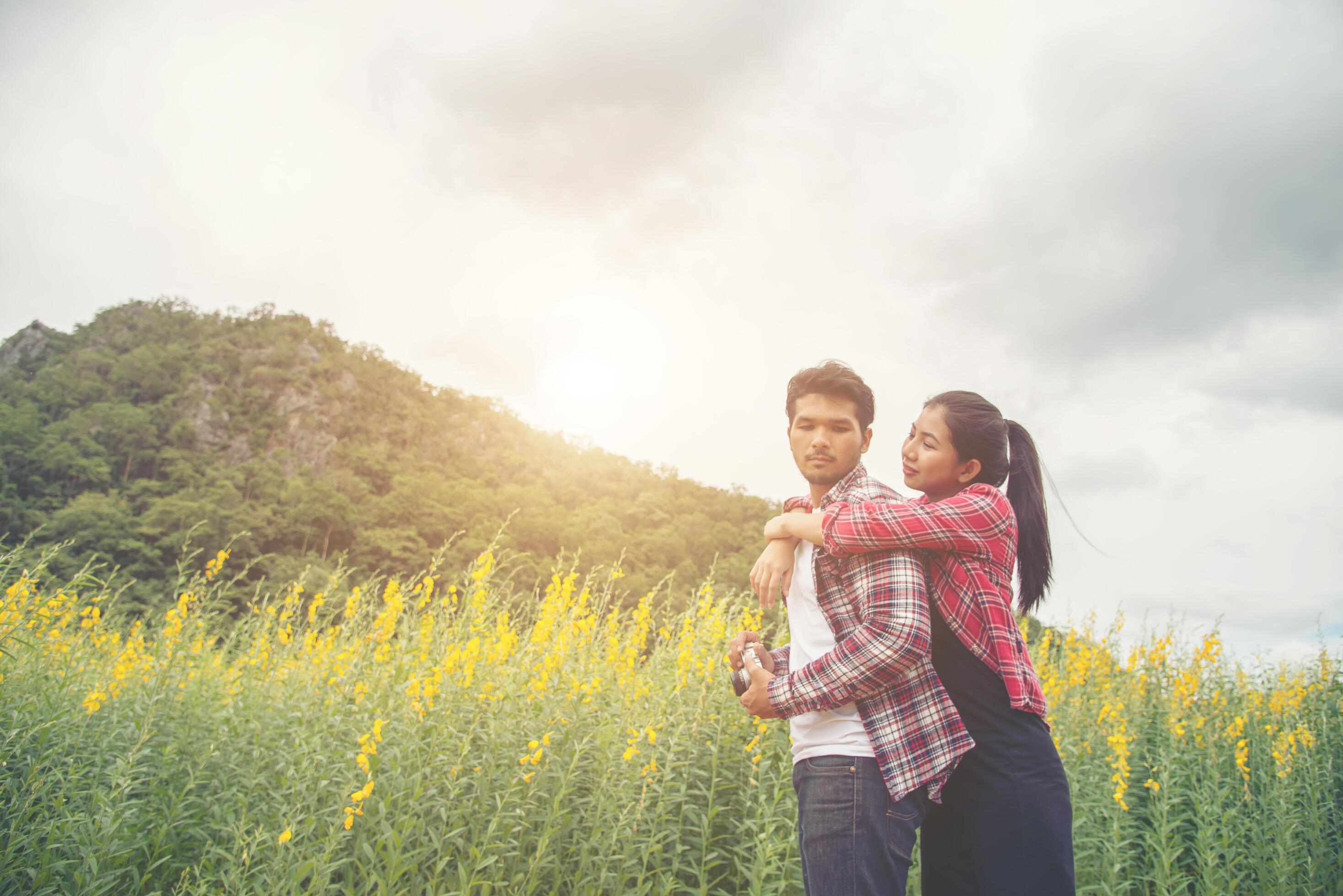 Young hipster couple relaxing in yellow flower field at summer. Enjoying with nature. Stock Free