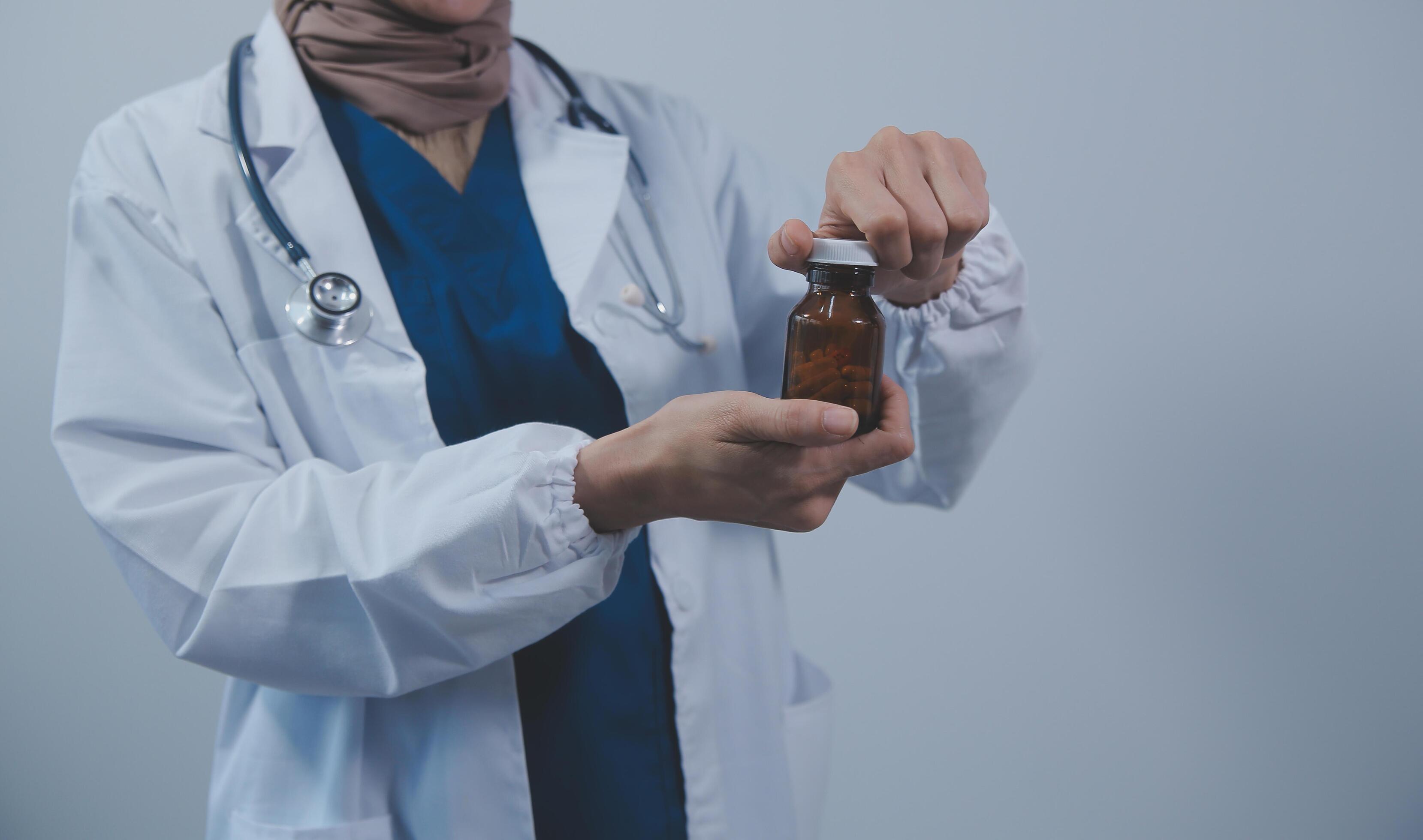 Southeast Asian medical doctor holding a bottle of pills, smiling isolated white background Stock Free