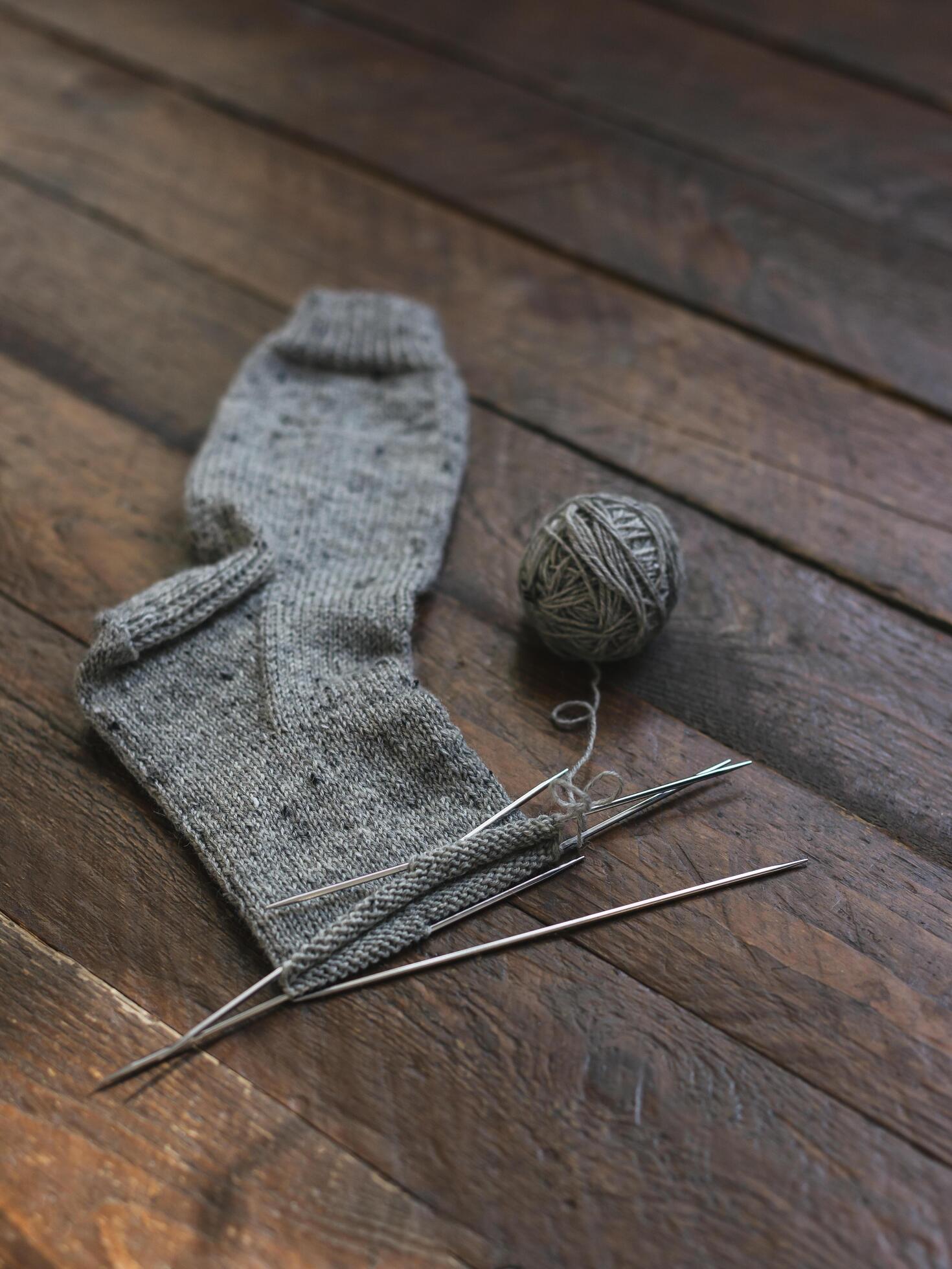 Hand knitted sock with needles and grey yarn ball on dark wooden background. Stock Free