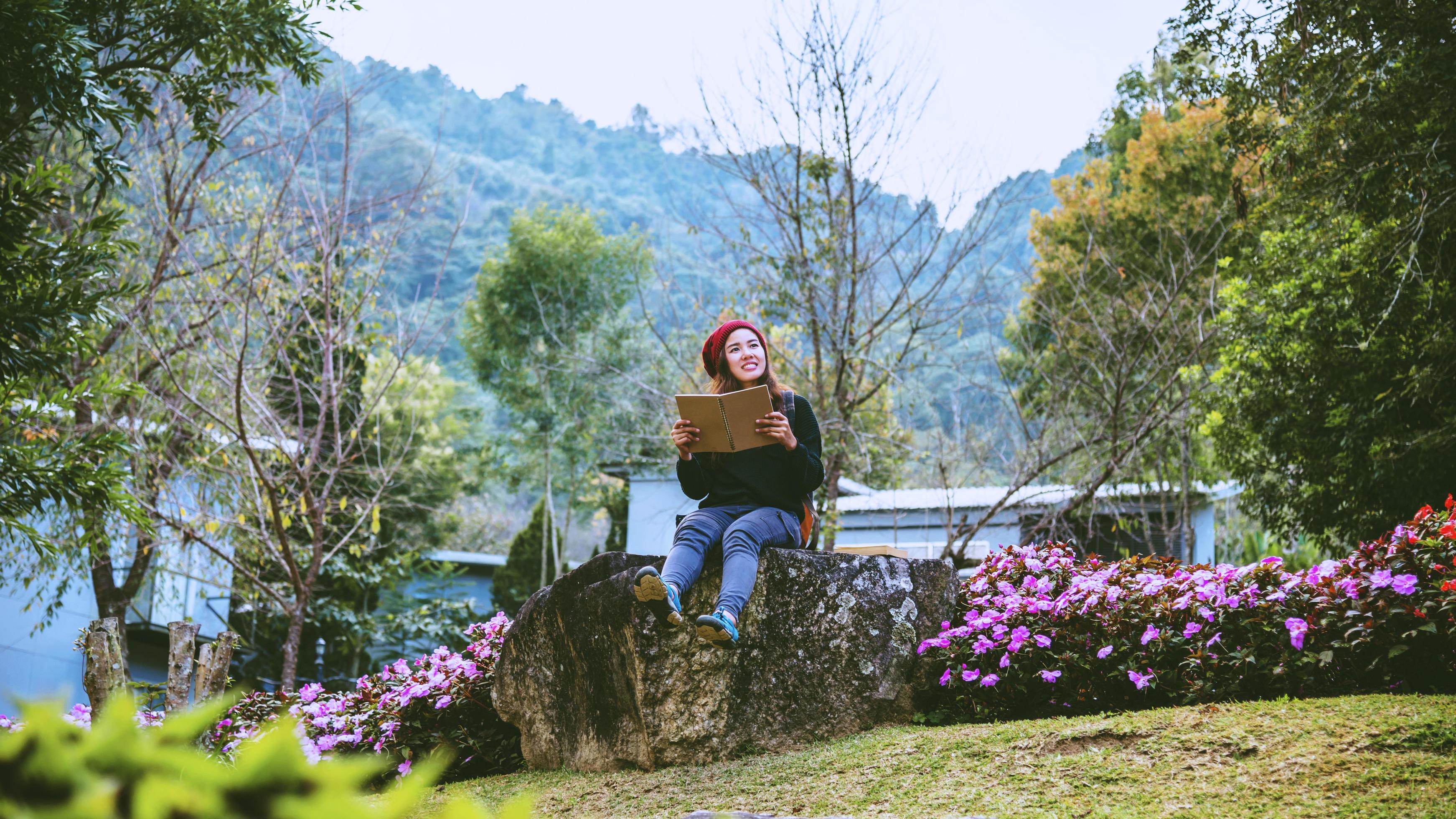 woman travel nature in the flower garden. relax sitting on rocks and reading books In the midst of nature at doi Inthanon. Stock Free