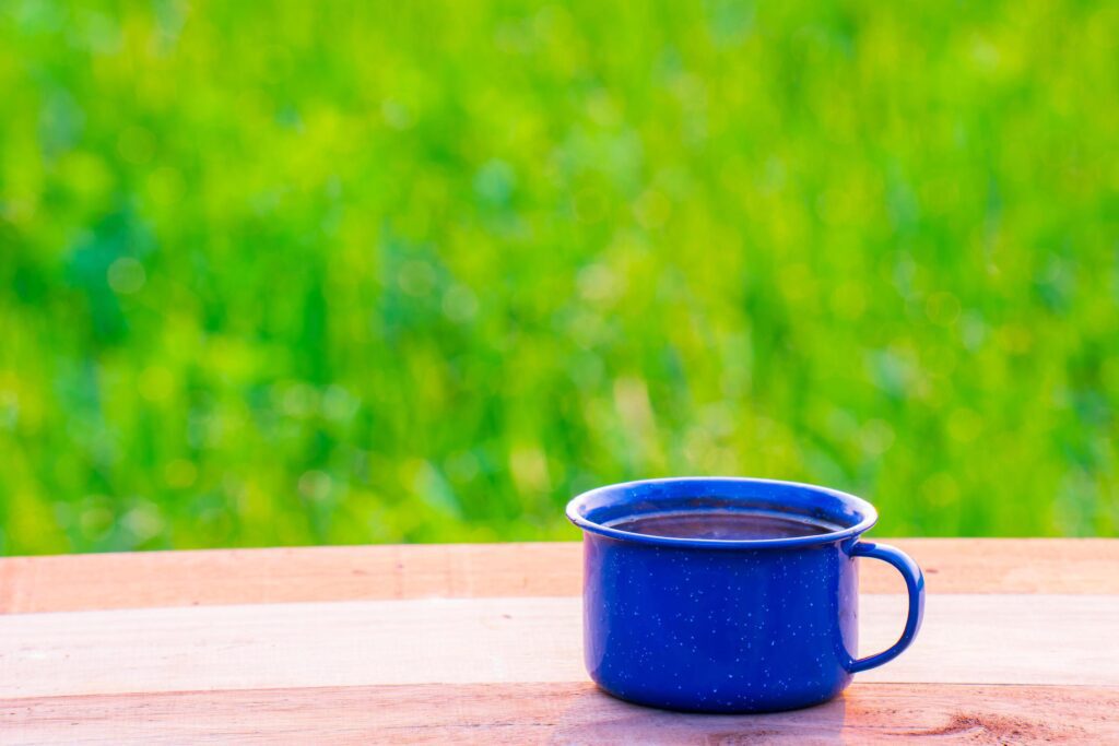 Kettle, blue enamel, and coffee mugs On an old wooden floor, Blurred background of rice fields at sunrise. Stock Free