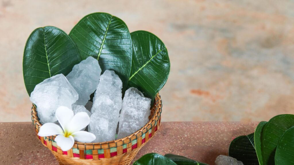 A basket filled with white alum crystals sits on a vibrant green shrub background. Stock Free