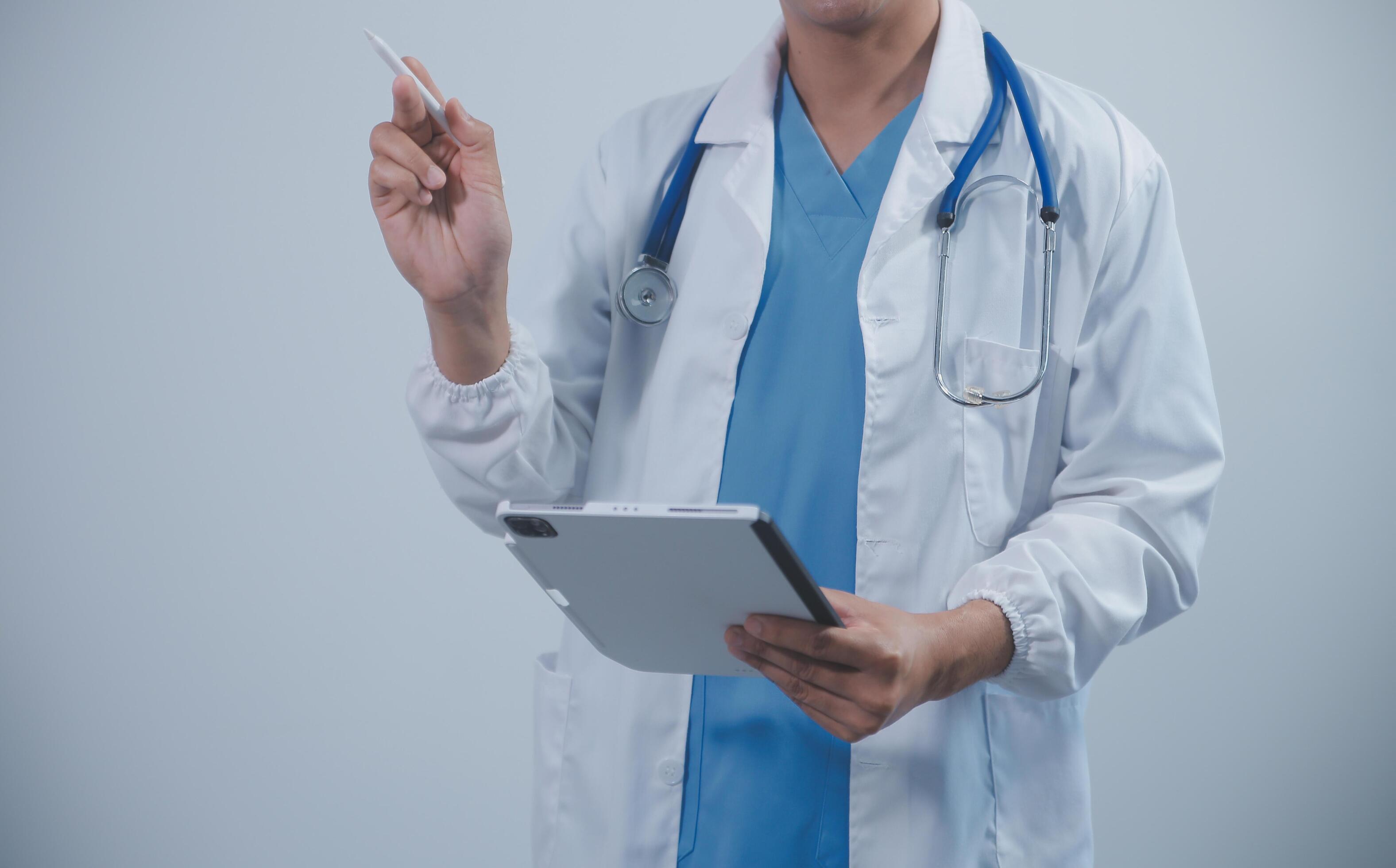 Mature male doctor with tablet pc is giving presentation. Blurred background indoors. Stock Free