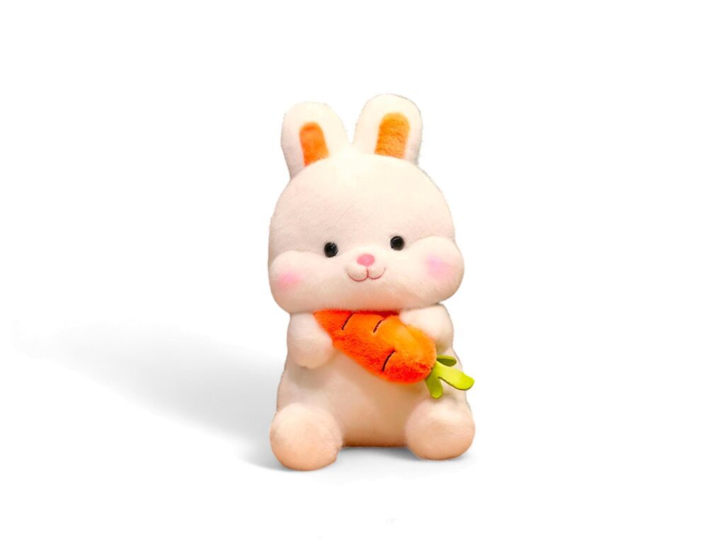 Cute stuffed rabbit holding a carrot on a white background Stock Free