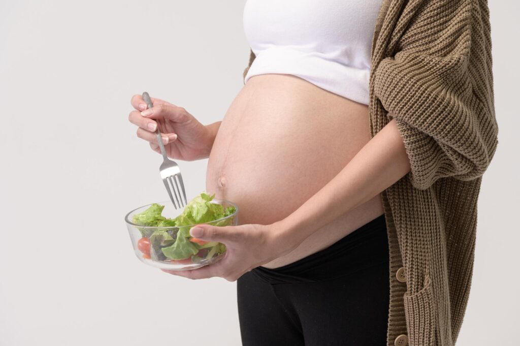 Portrait of Beautiful pregnant woman eating salad over white background studio, health and maternity concept Stock Free