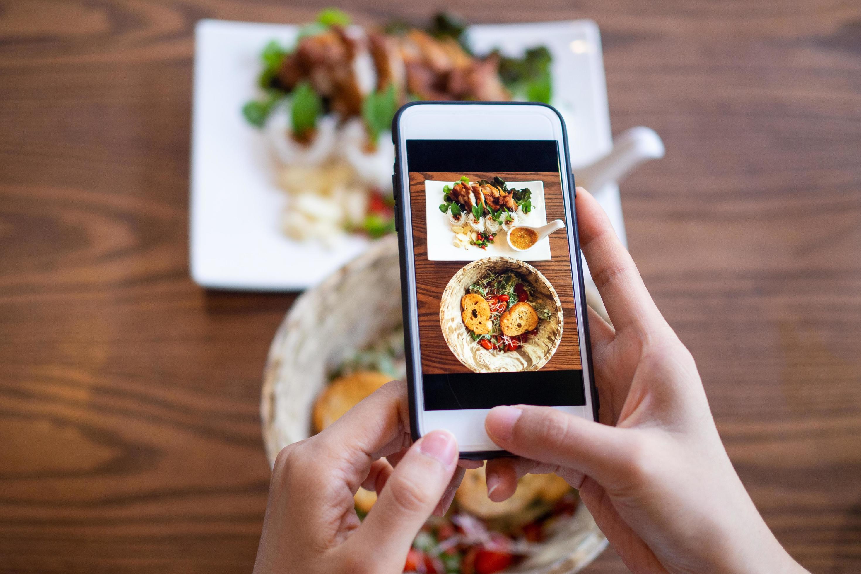 The hand of a woman using a mobile phone to take pictures of food on the table to review and upload to social networks Stock Free