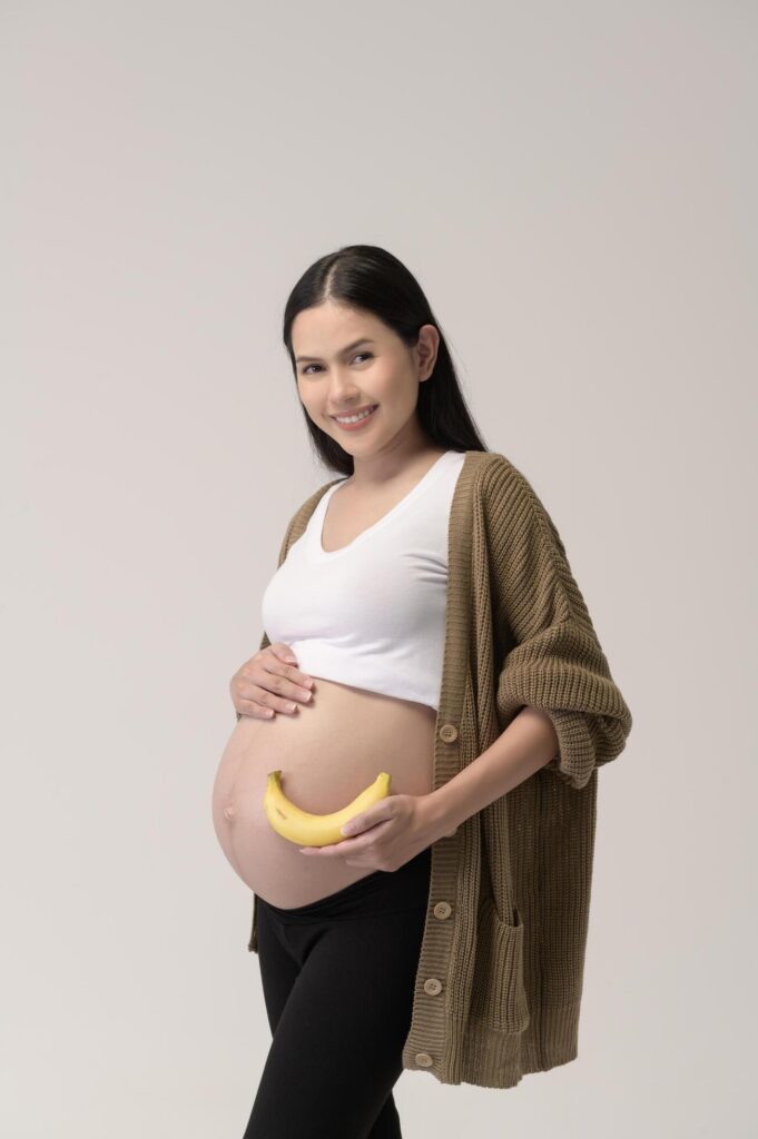 Portrait of Beautiful pregnant woman holding banana over white background studio, health and maternity concept Stock Free