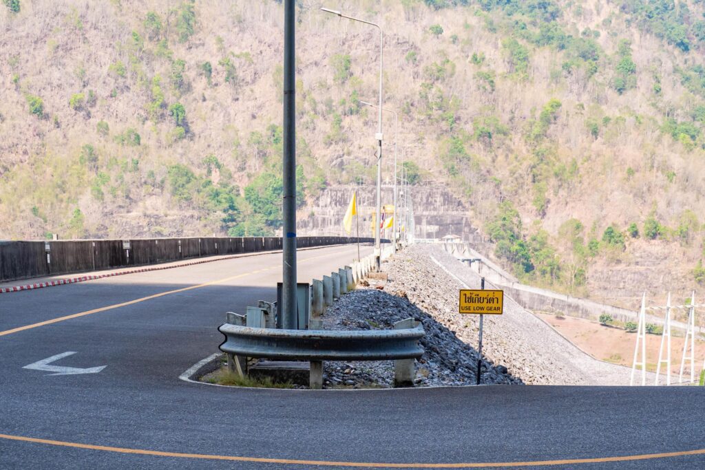 The scene of the road at the top of the dam, with the mountains in the background and a light pole. Stock Free