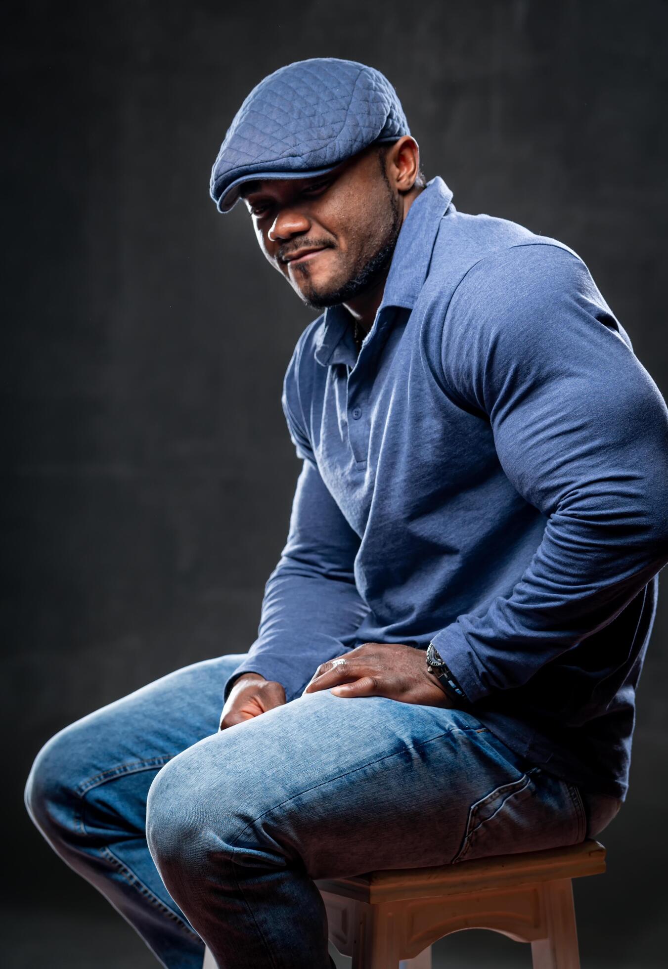 Strong african american in total denim clothes sits on chair and poses to the camera on black background. Closeup. Concept photo. Stock Free