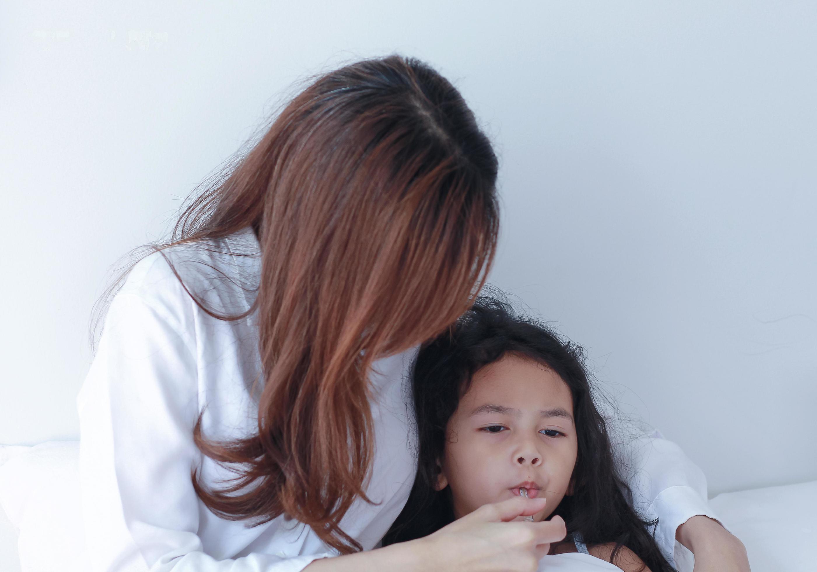 Asian mother measuring temperature of her daughter Stock Free