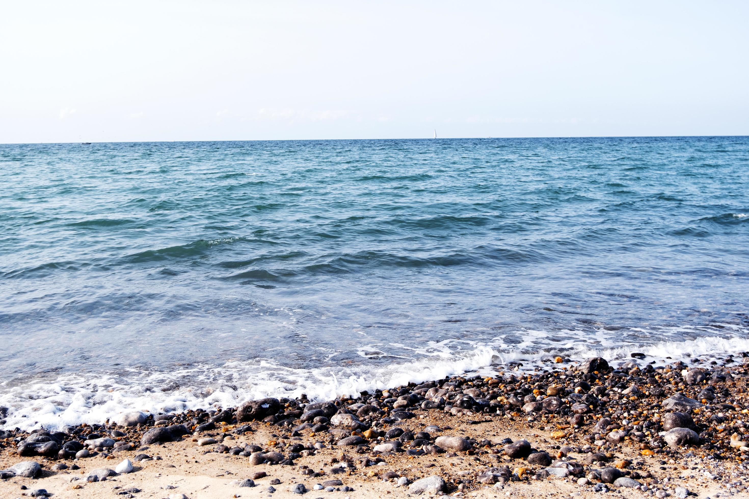 Tender ocean waves and pebbles on the coast line, blue sea waters on a sunny day, beautiful seascape natural background Stock Free