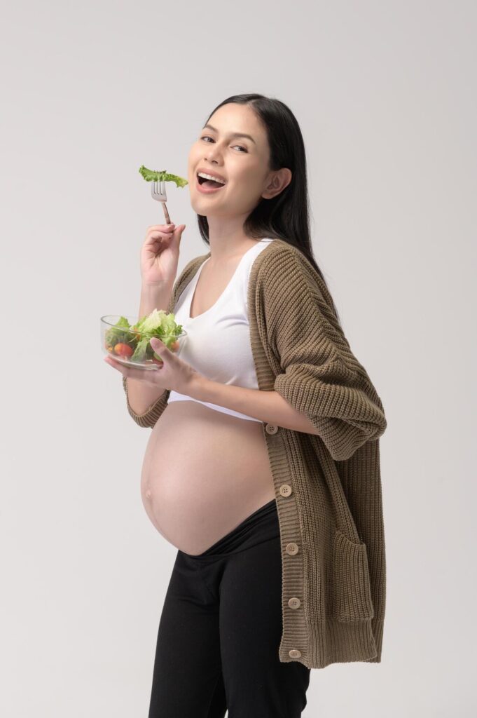 Portrait of Beautiful pregnant woman eating salad over white background studio, health and maternity concept Stock Free