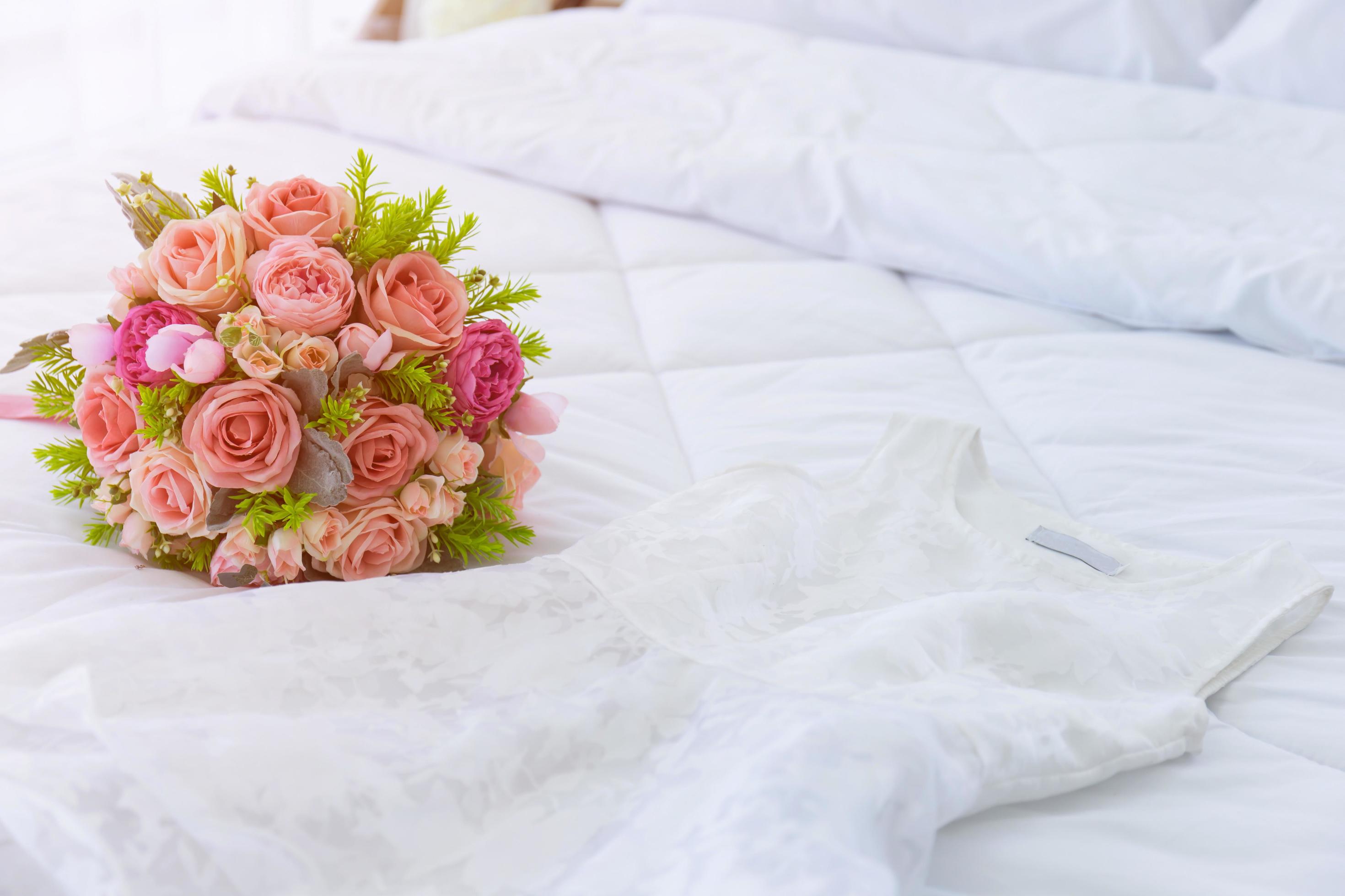 A beautiful bouquet of flowers was laid out on a clean, white bed. Next to the bridal gown were placed together. Stock Free