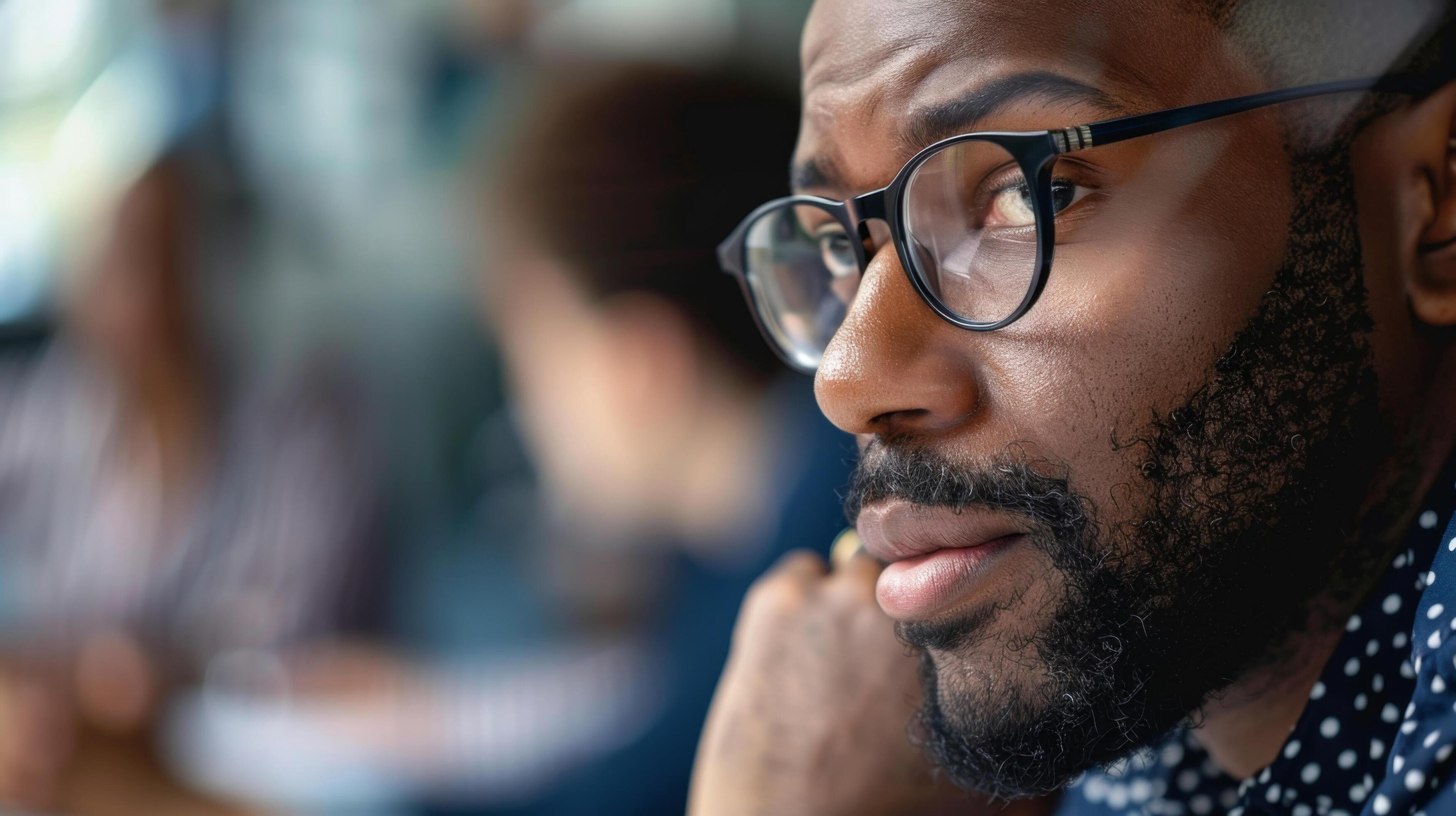 Close-up of a thoughtful man with glasses and a beard in an office setting. Ideal for professional and business-related themes. Stock Free