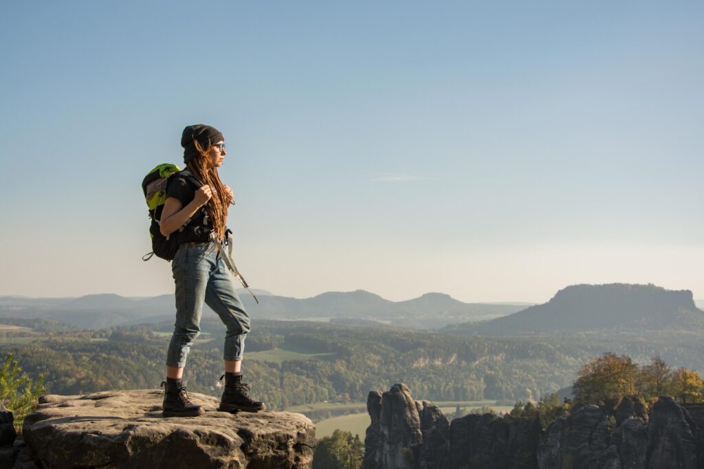 Young woman traveler with baclpack stand on the cliff in mountains Stock Free