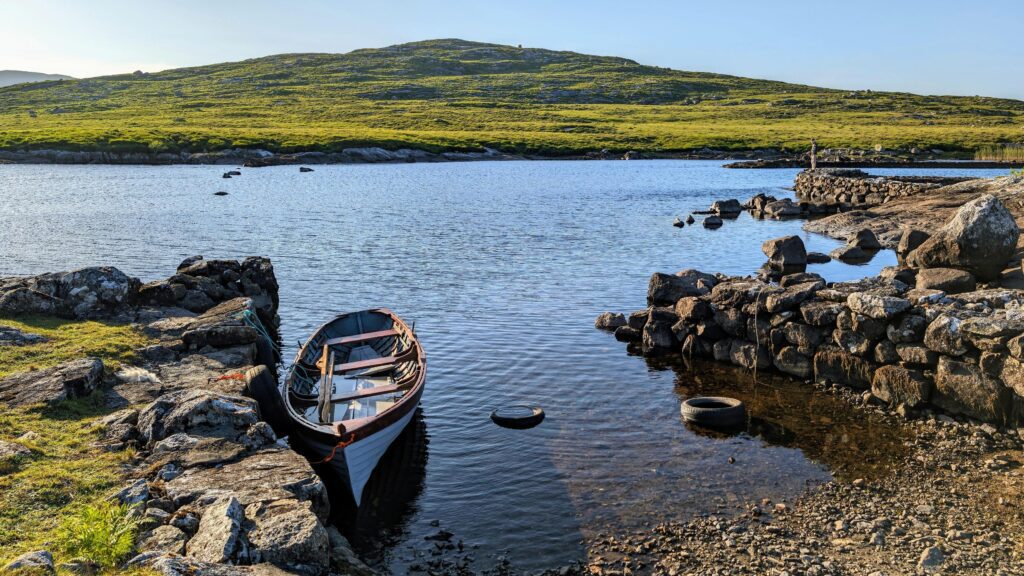 Old wooden fishing boat in lake by Fisherman’s hut with mountains in background at Connemara, Galway, Ireland Stock Free