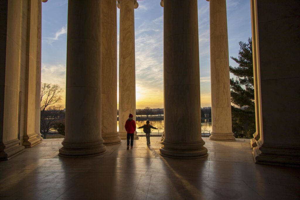 Children playing near giant pillars at a monument when the sun is setting Stock Free