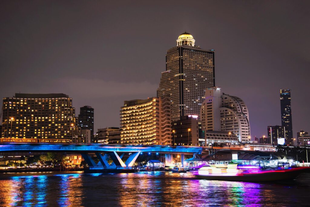 Colorful night picture of Asian city – blue light bridge over big river and building background in Bangkok Thailand Stock Free