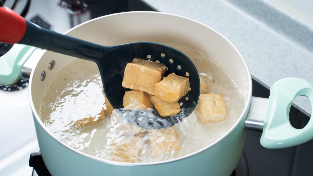 Cooking diced cubed dried tofu on gas stove in home kitchen, lifestyle, closeup. Stock Free