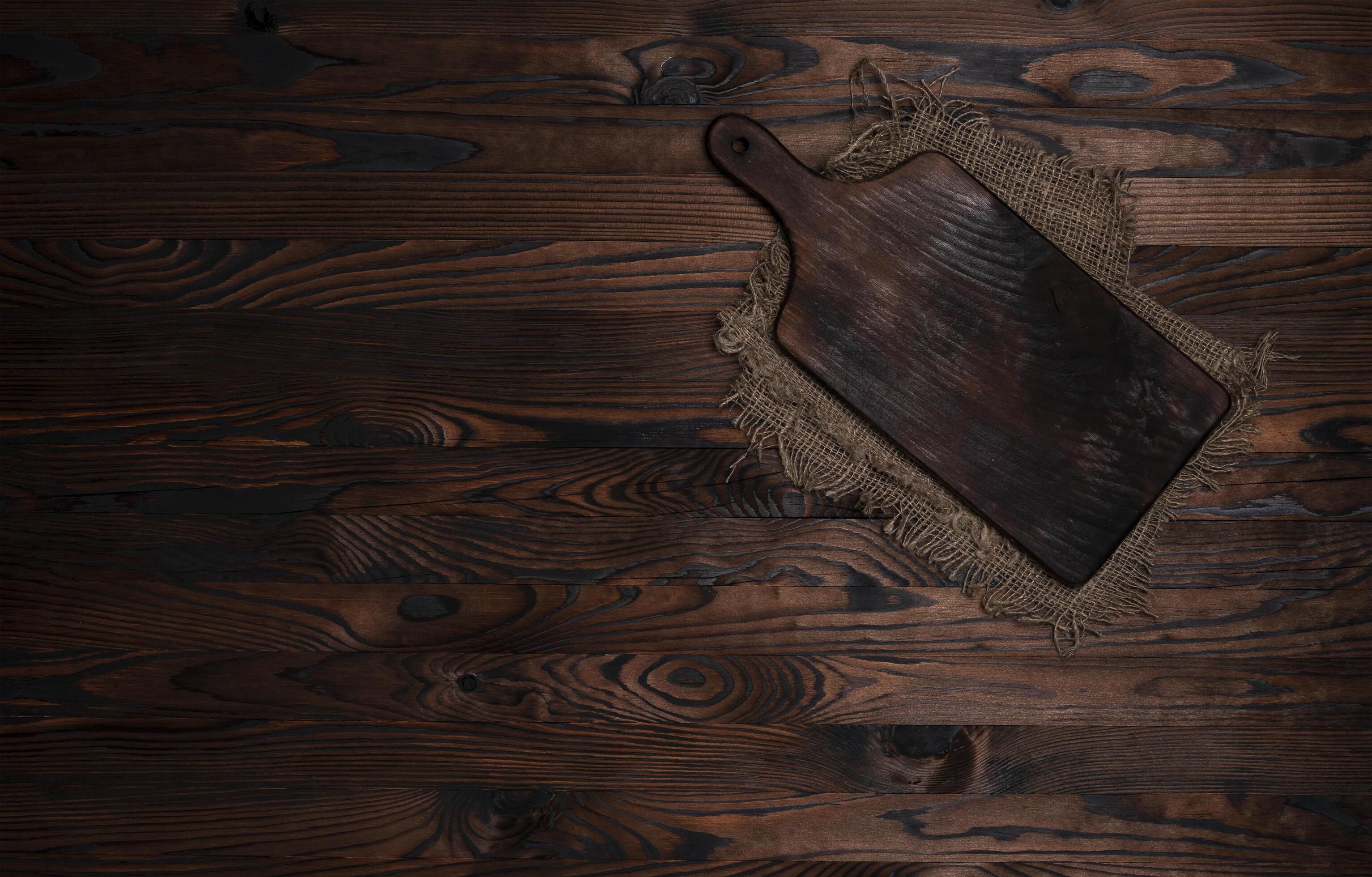 Cutting board with burlap napkin on brown wooden background, top view Stock Free