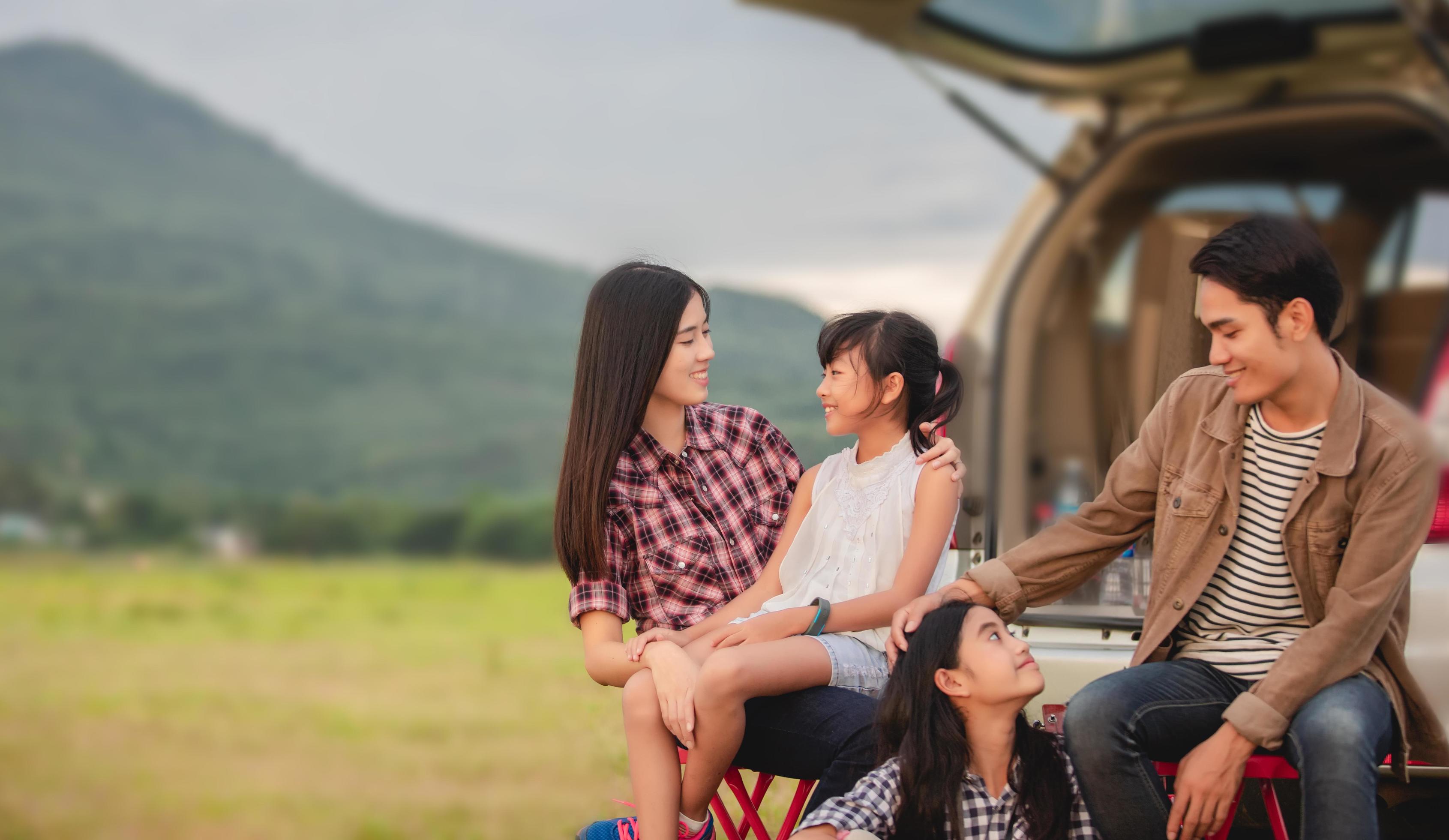 Happy little girl with asian family sitting in the car for enjoying road trip and summer vacation in camper van Stock Free